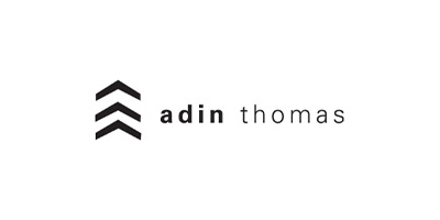 The image shows a logo with text that reads 'adin thomas' set against a gray background.